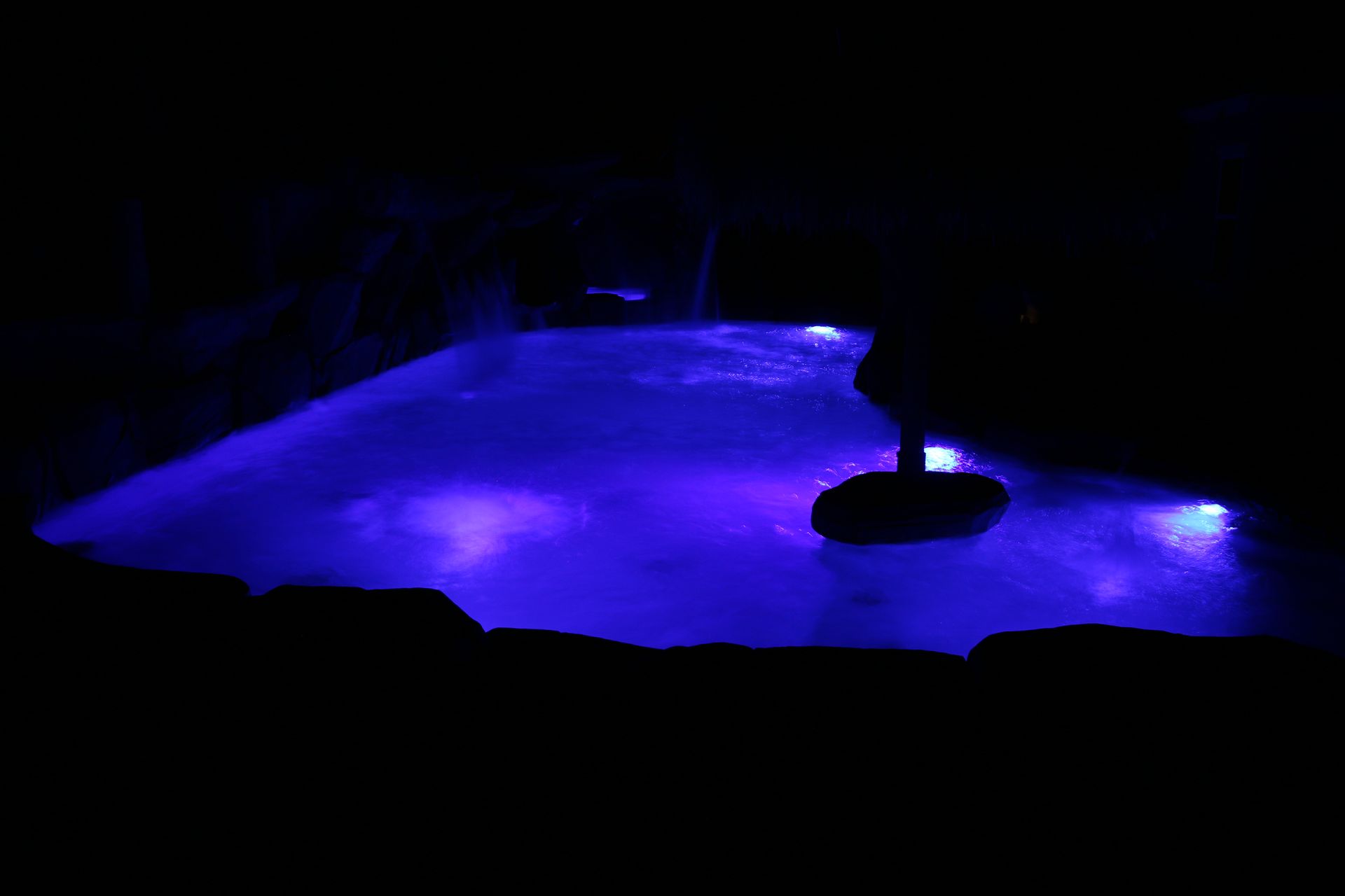A swimming pool illuminated by bright blue underwater lights at night.