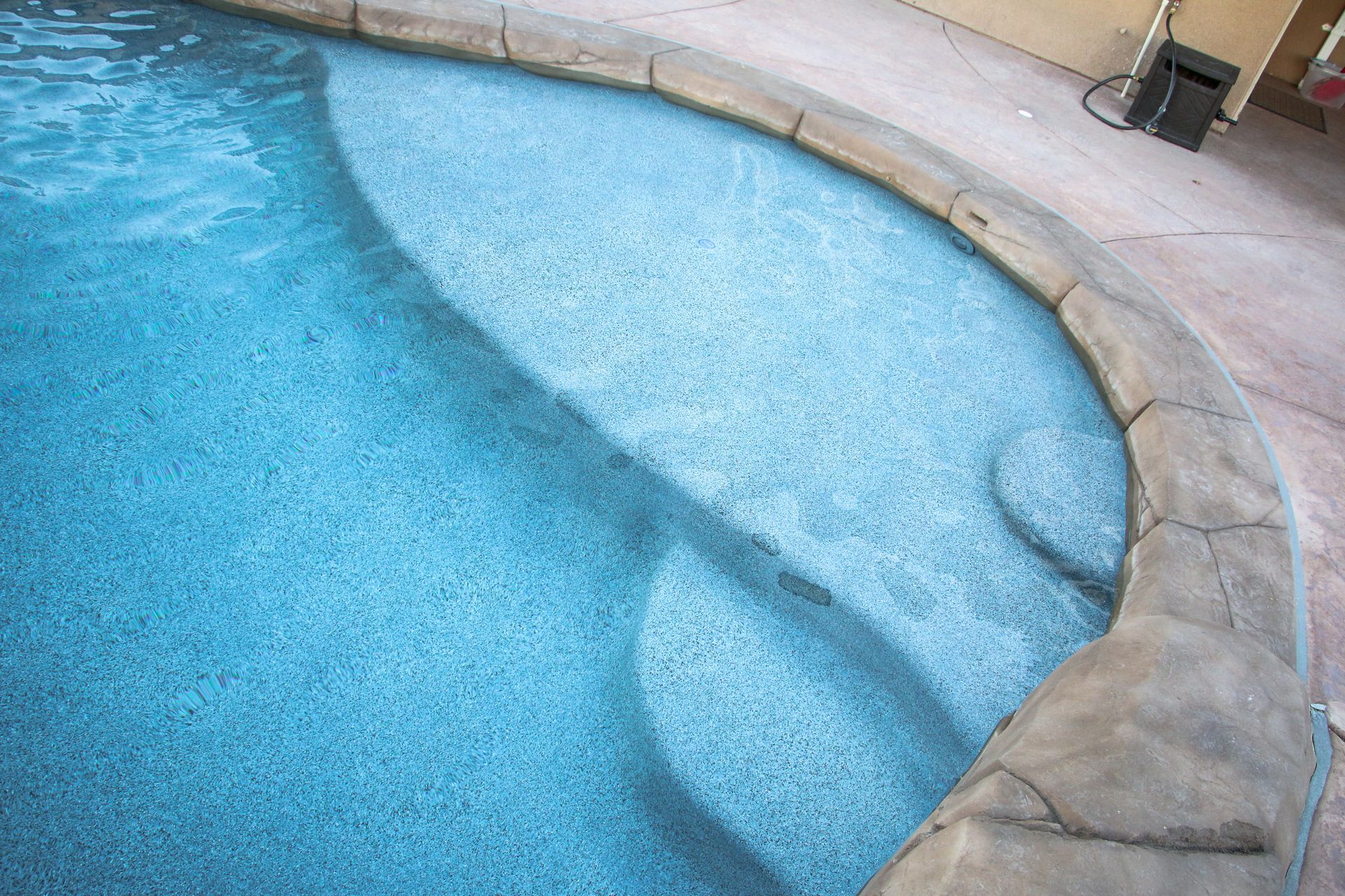 A blue swimming pool corner featuring integrated steps and a textured, stone-colored coping edge.