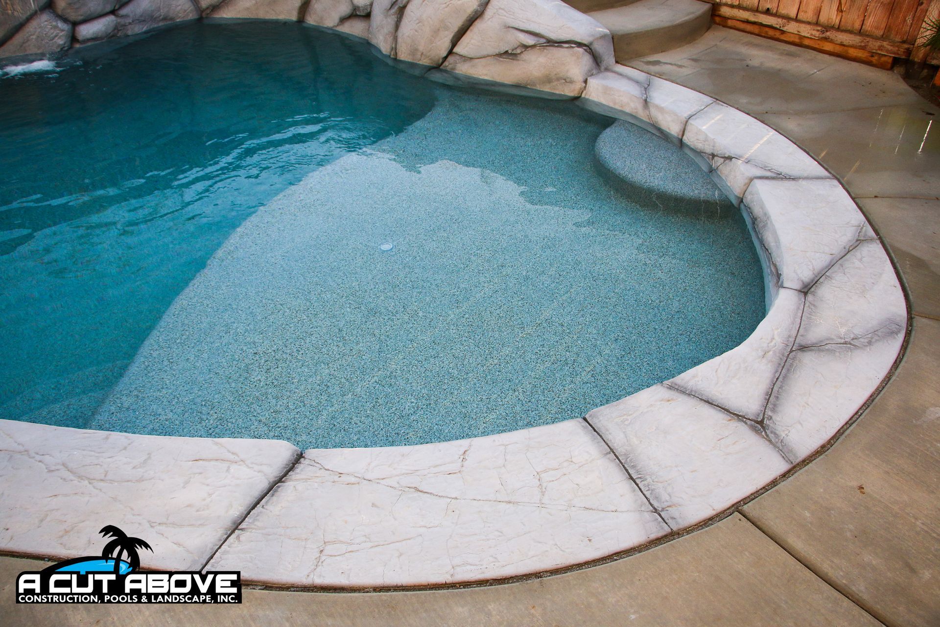 A curved swimming pool with a stone-textured coping border and a built-in step feature.