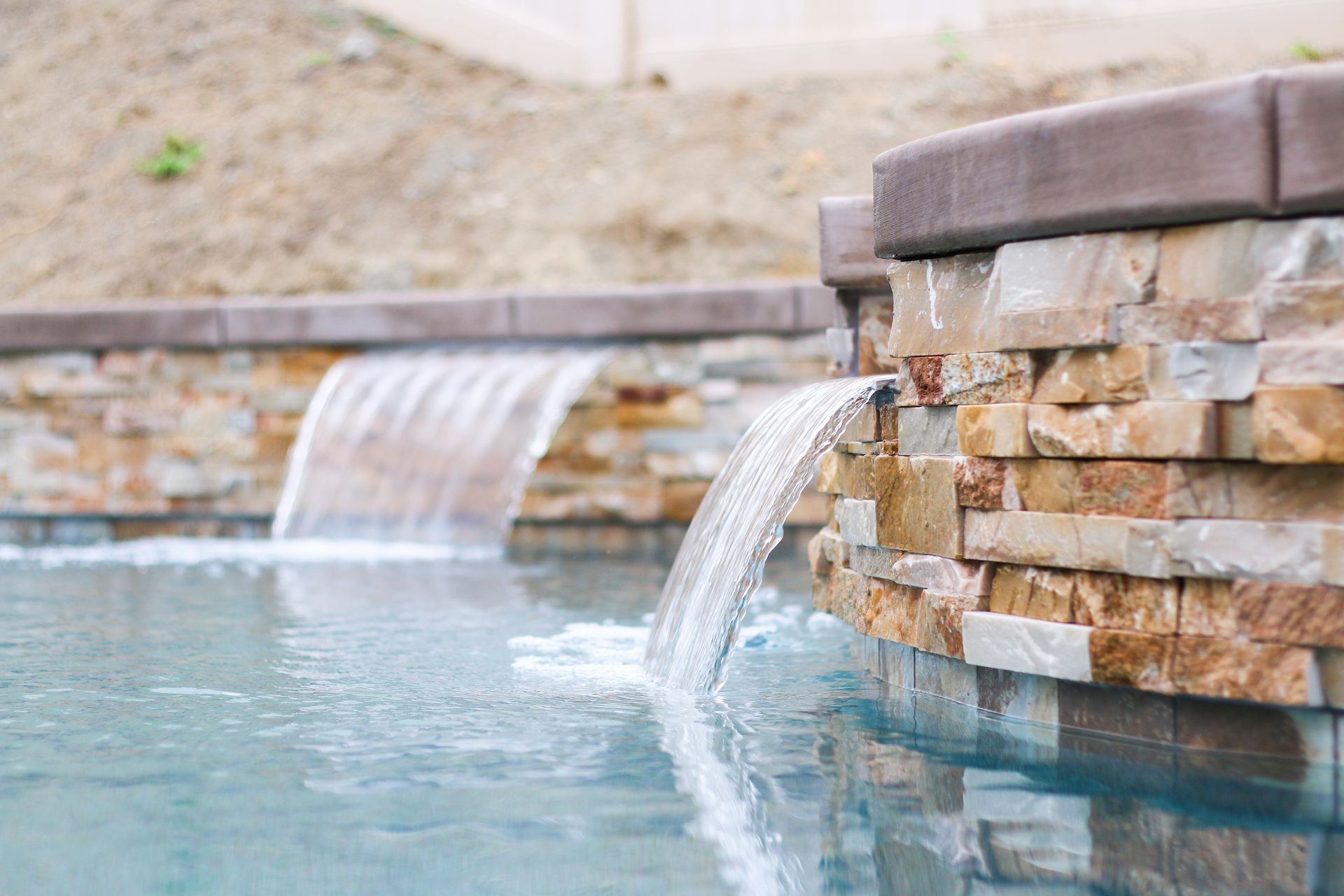 Two stone water features pouring streams of water into a backyard swimming pool.