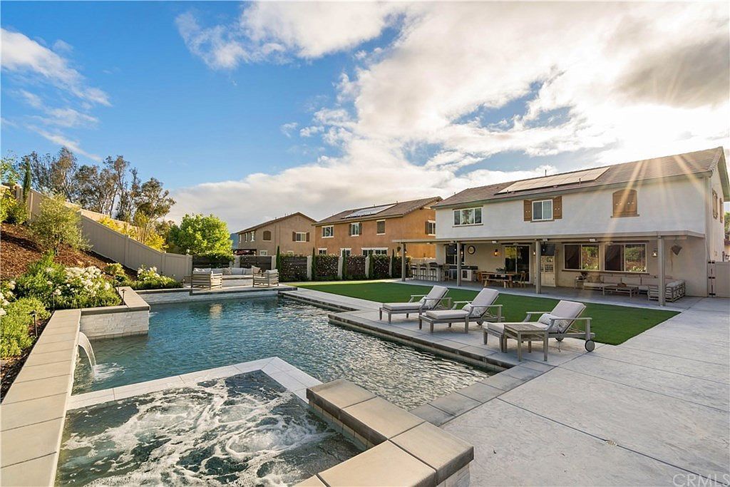 A backyard featuring a swimming pool, attached hot tub with jets, and lounge chairs on a patio beside a suburban house.