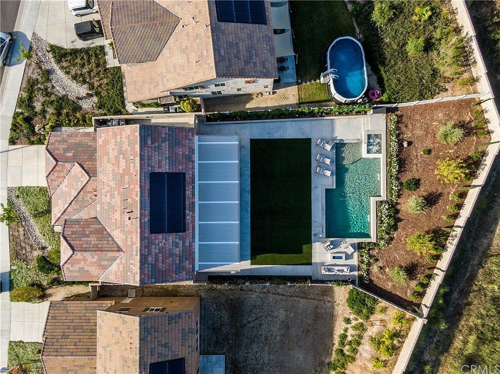 Aerial view of a residential backyard with a rectangular swimming pool, turf lawn, patio, and adjacent houses.