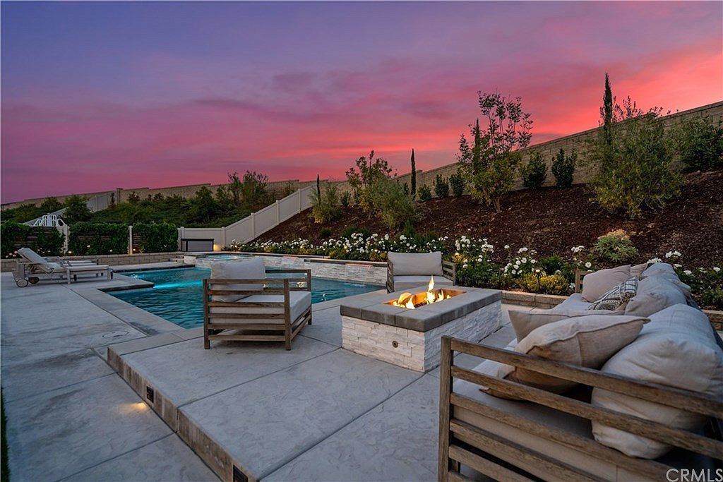 Luxury patio with a pool and fire pit at sunset, featuring stone flooring and comfortable outdoor lounge seating.