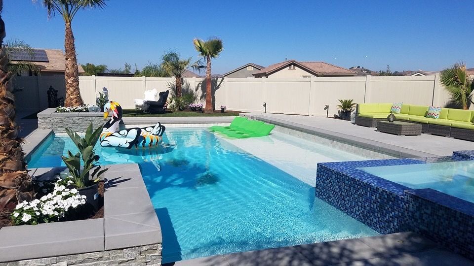 A swimming pool with a tiled spa and lounge area, featuring a blue water surface, palm trees, and modern outdoor furniture.