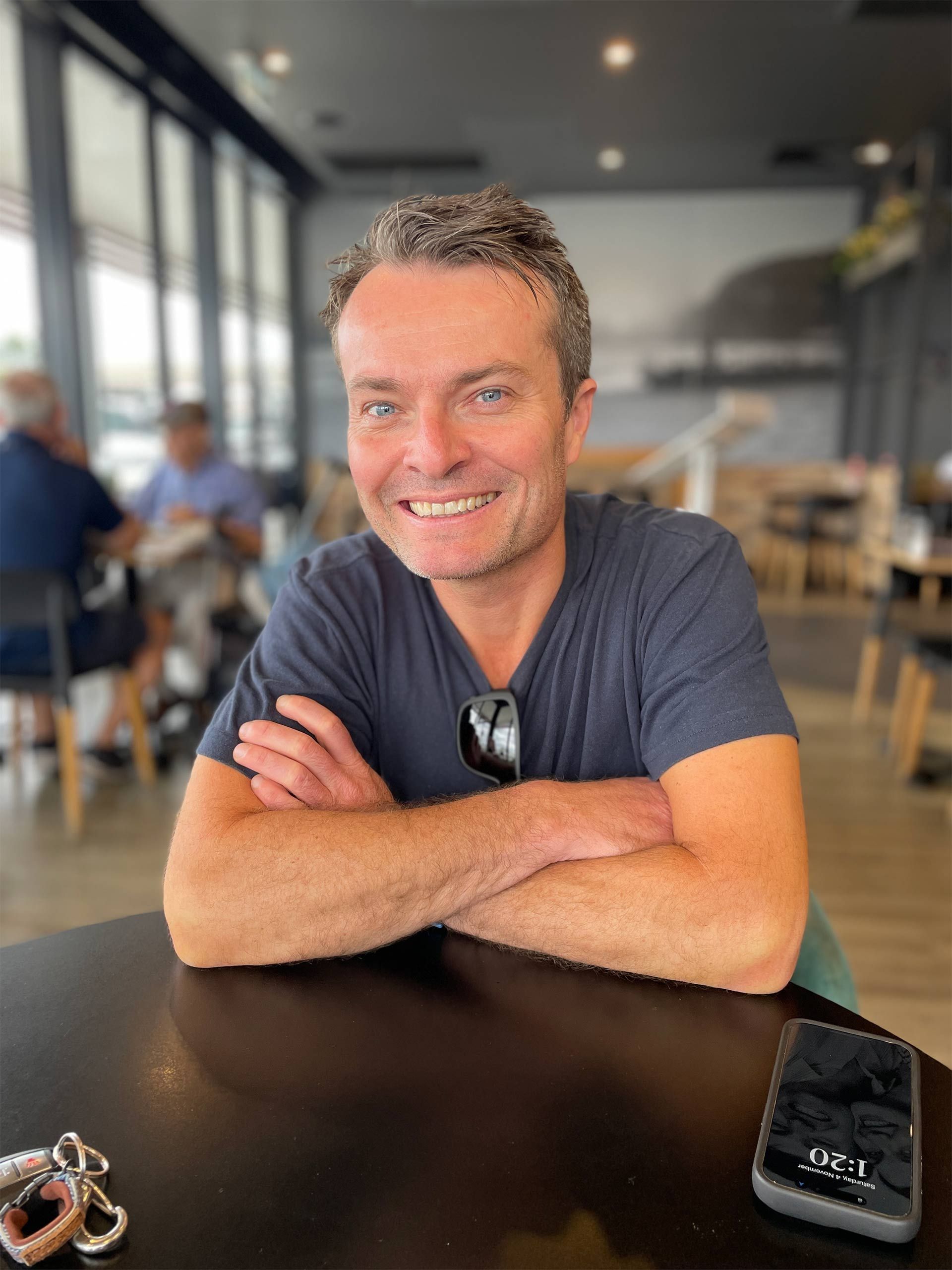 A man is sitting at a table with his arms crossed and smiling.