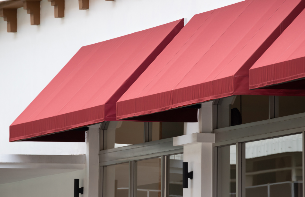 Auvents rouges au-dessus des portes et fenêtres vitrées d'un bâtiment blanc.