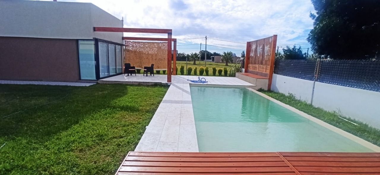 Una casa moderna con piscina y terraza de madera rodeada de césped. Cielo nublado.