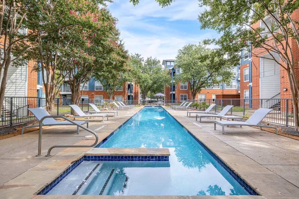 a large swimming pool surrounded by chairs and trees in front of a building at Marquis on Gaston in Dallas, TX.