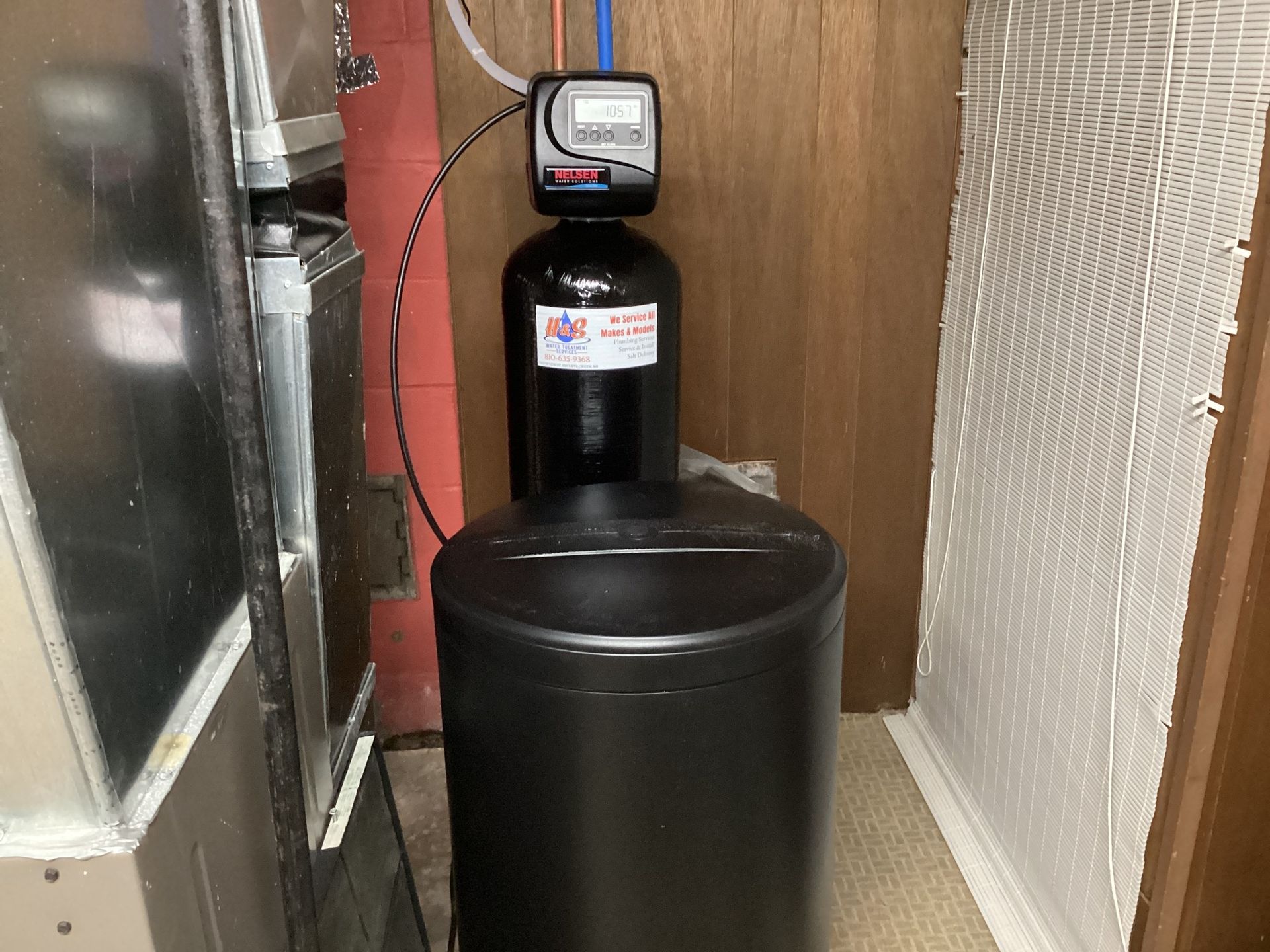 A black water softener is sitting in a corner of a room.