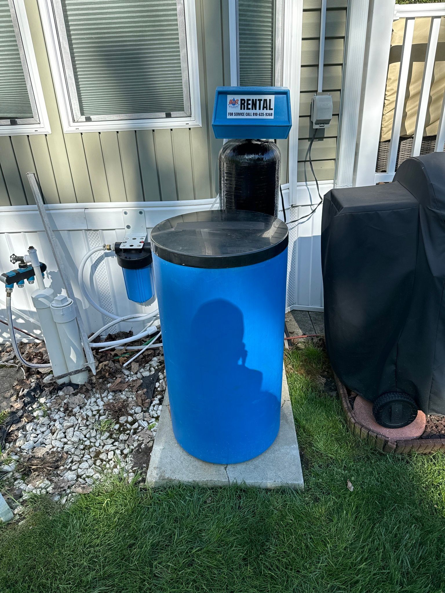 A blue water softener is sitting in the grass in front of a house.