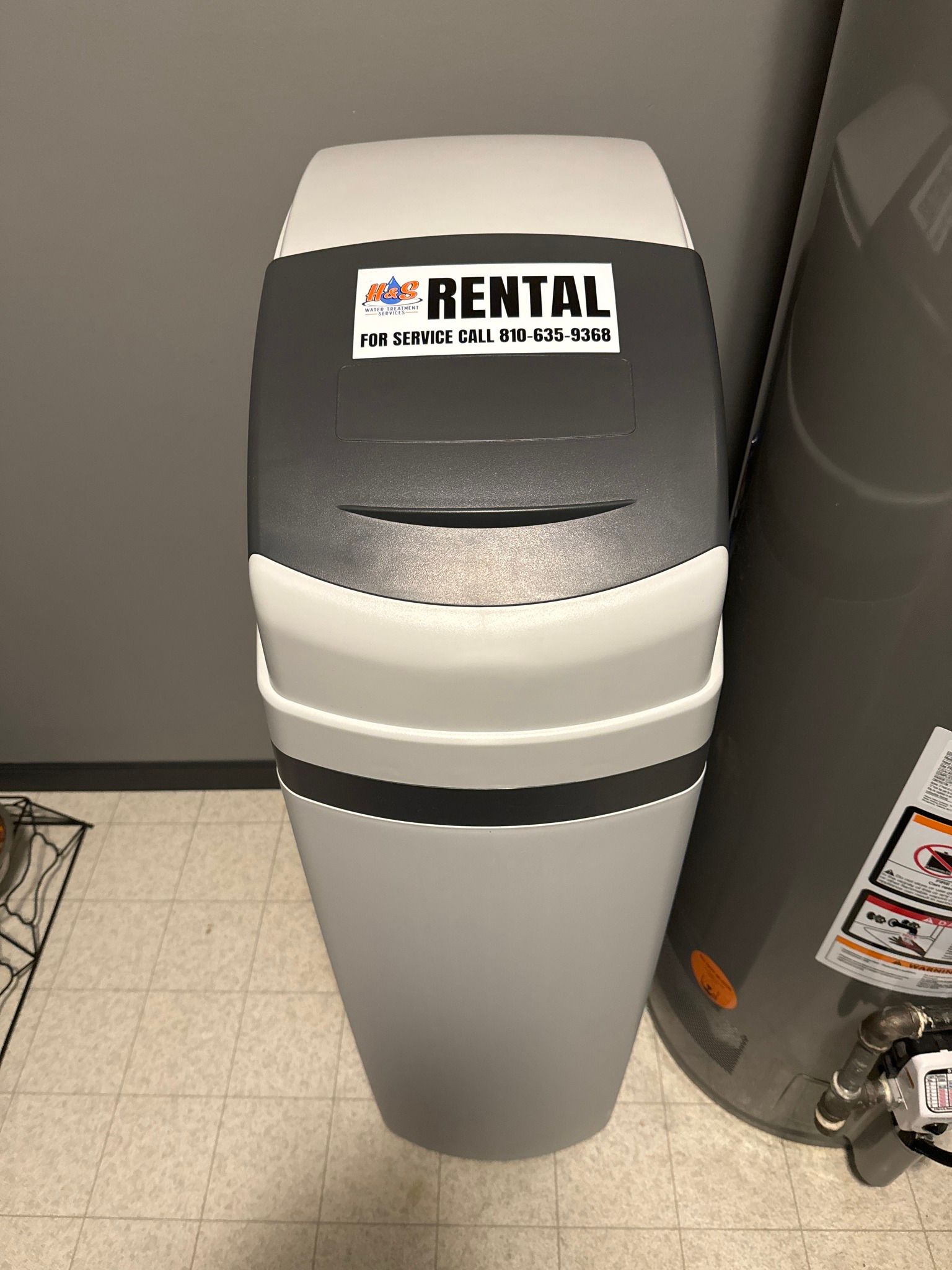 A water softener is sitting next to a water heater in a bathroom.