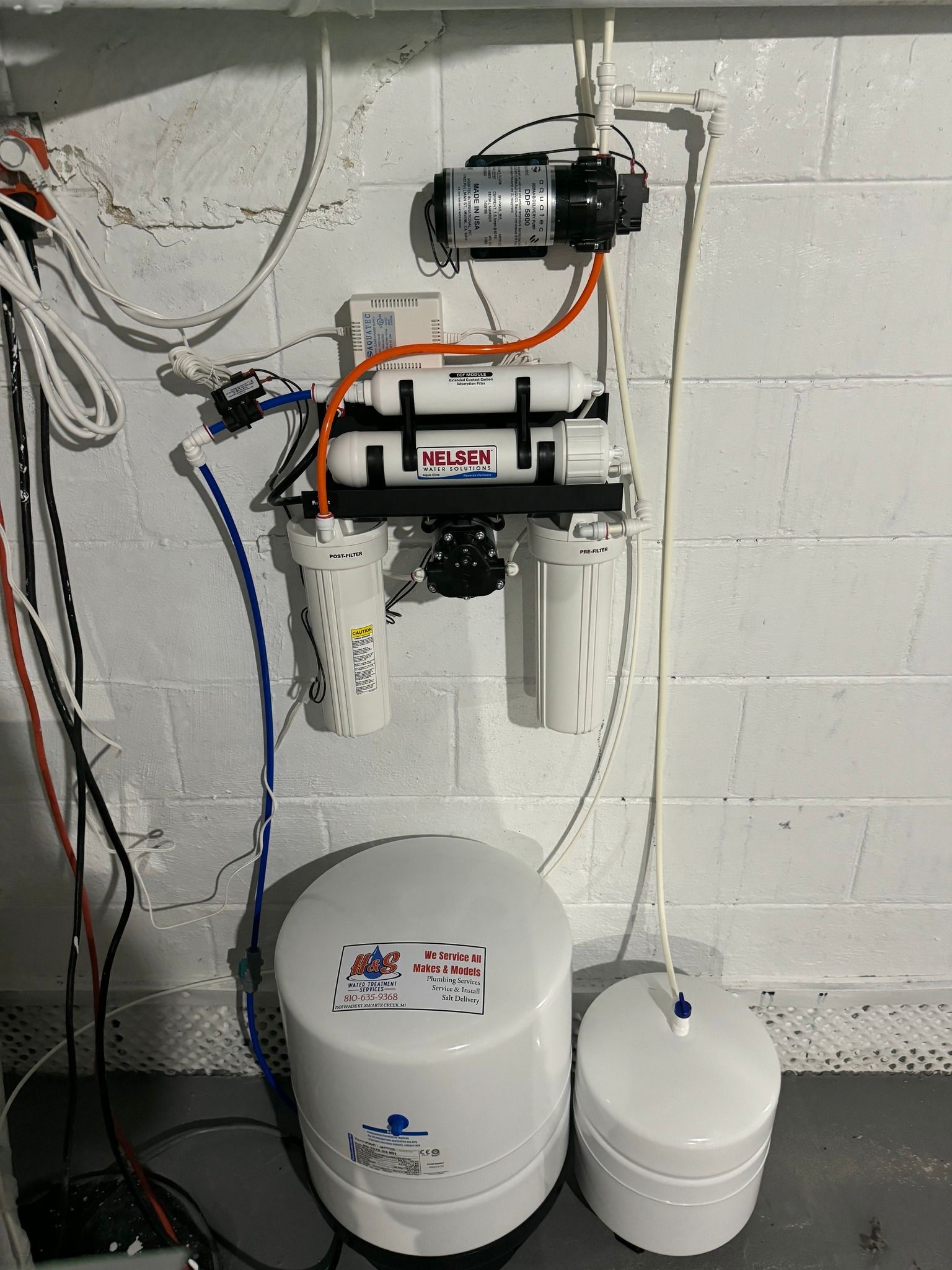 A water filter is installed on a brick wall in a basement.