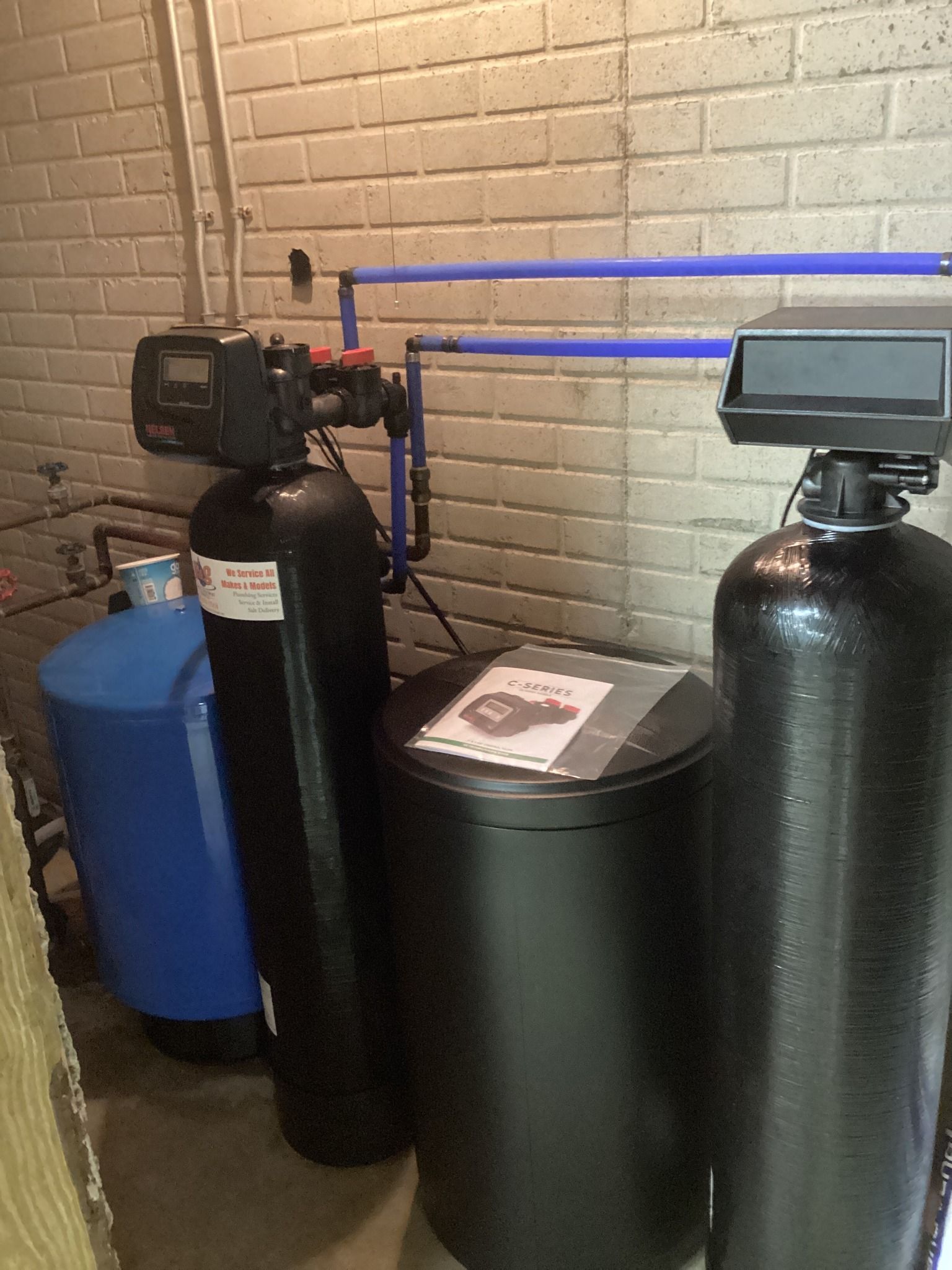 Two water softeners are sitting next to each other in a room next to a brick wall.