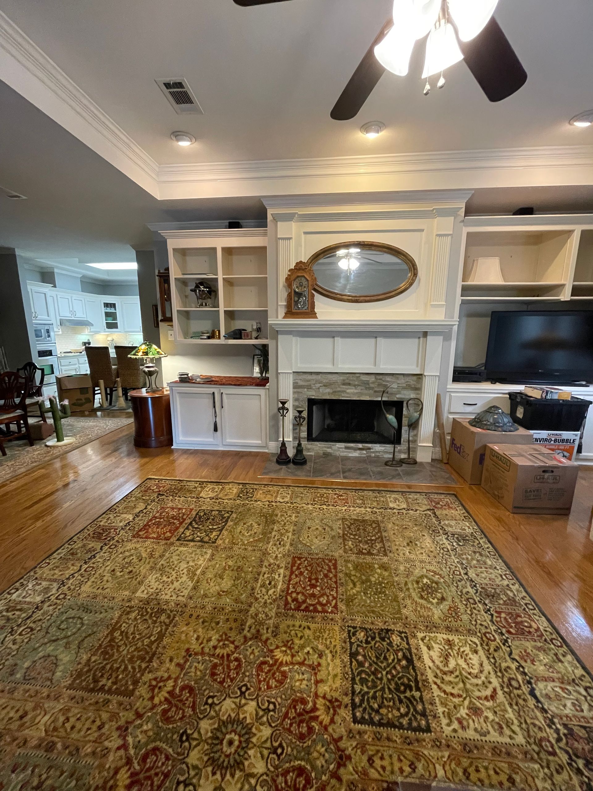 Living room with built-in shelves, fireplace, large patterned rug, hardwood floors, and a ceiling fan.