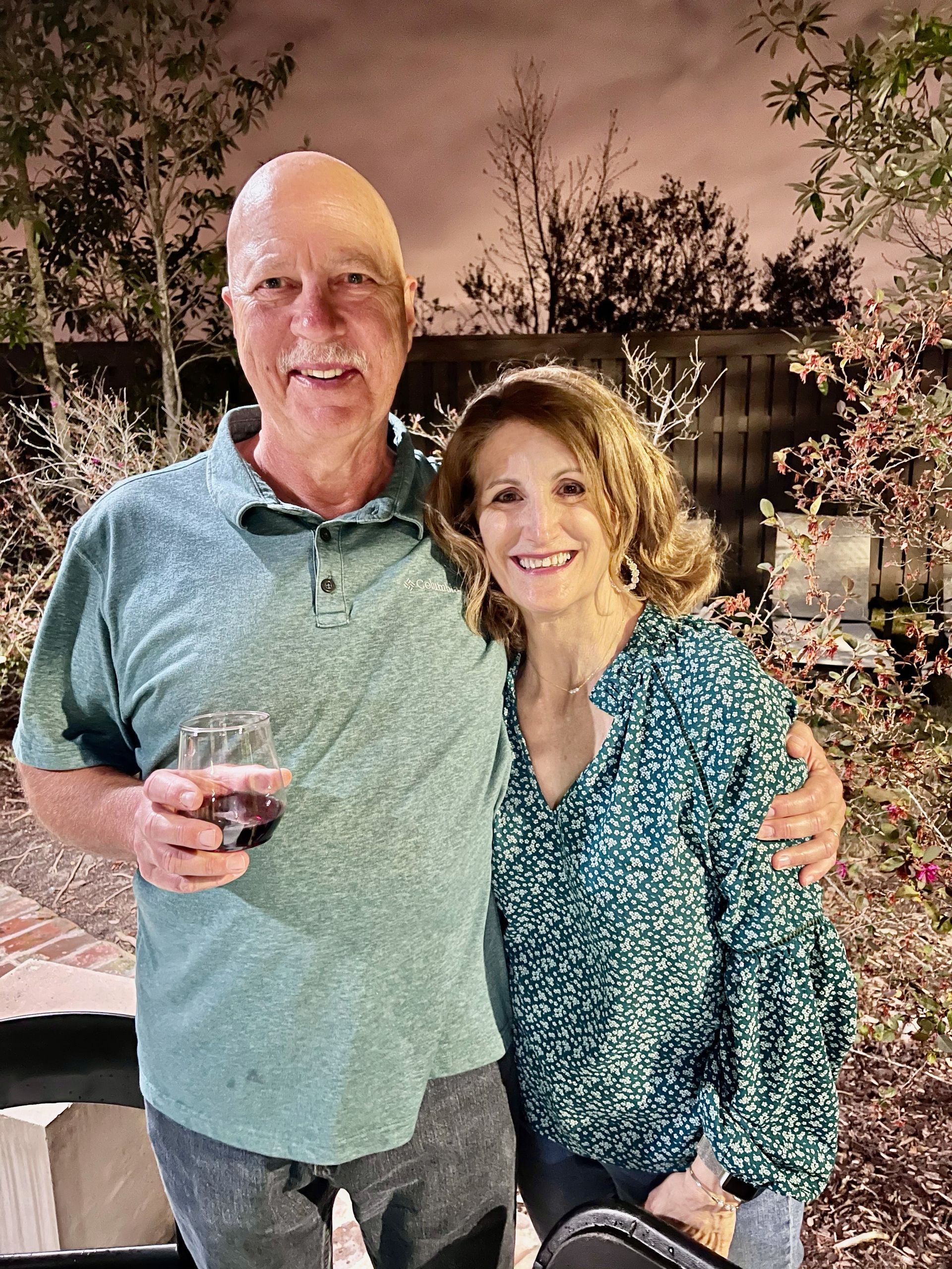 A man and a woman are posing for a picture while the man is holding a glass of wine.