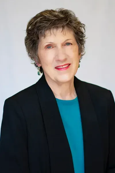 A woman wearing a black jacket and a blue shirt is smiling for the camera.