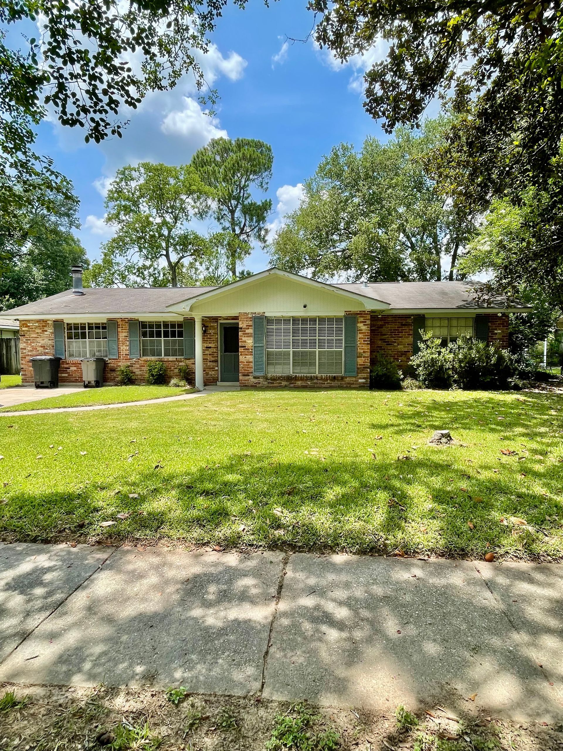 Brick ranch house with green lawn and trees on a sunny day.
