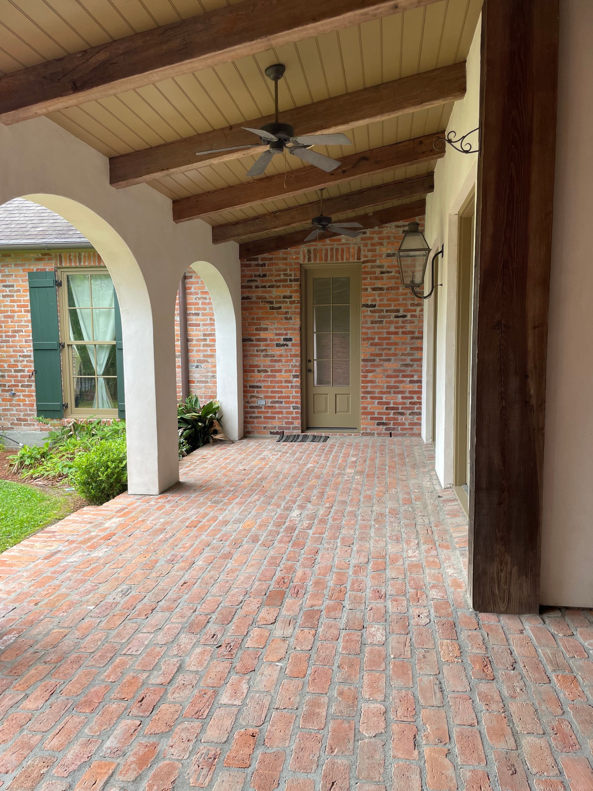 Brick-covered covered patio with arches, wooden ceiling, and a ceiling fan overlooking a small courtyard.
