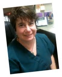 A woman in a blue scrub top is sitting in a chair and smiling.