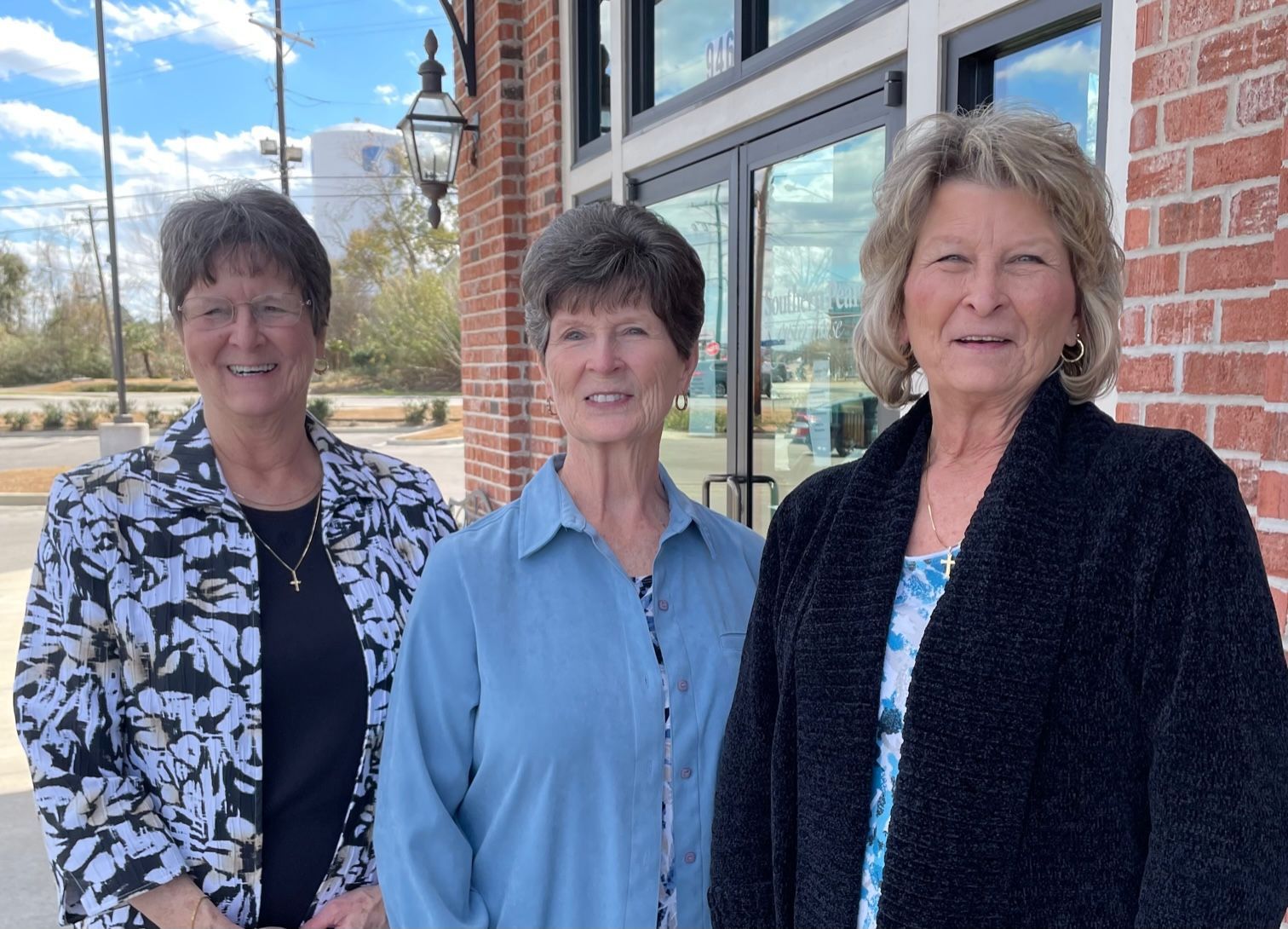 Three women are posing for a picture in front of a brick building.
