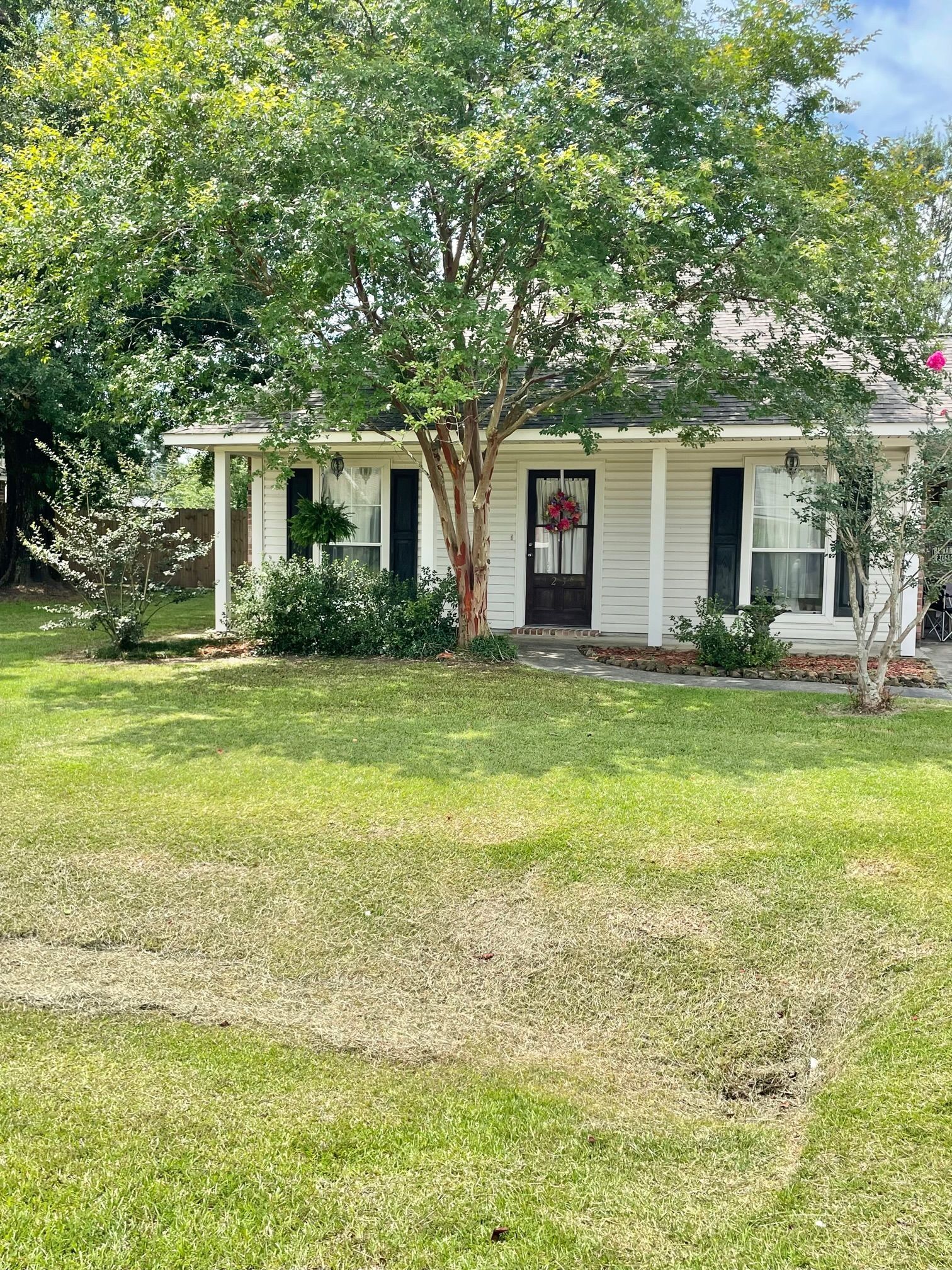 A white house with a porch and a large lawn in front of it.