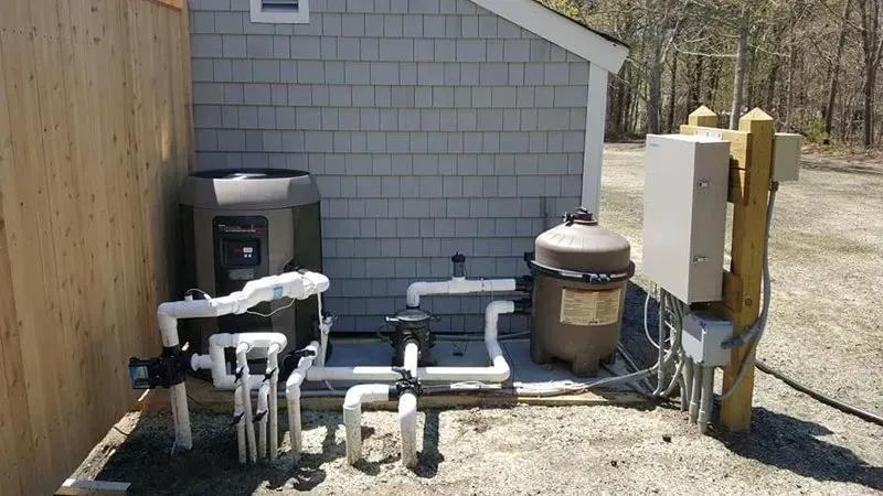 A swimming pool pump is sitting outside of a shed.