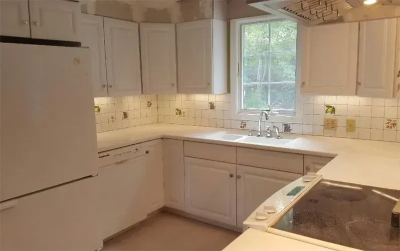A kitchen with white cabinets and appliances and a window