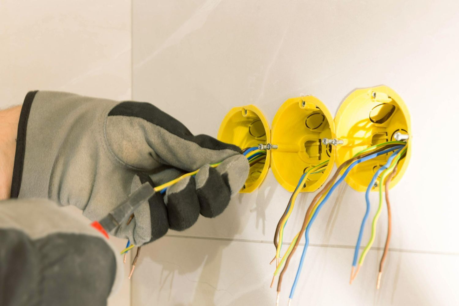 Electrician installing wiring into yellow electrical boxes on a white wall.