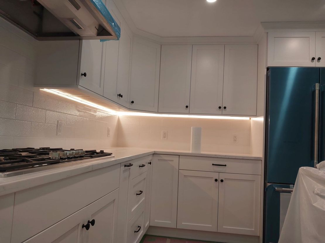 White kitchen cabinets with under-cabinet lighting. Stainless steel appliances and white countertops.