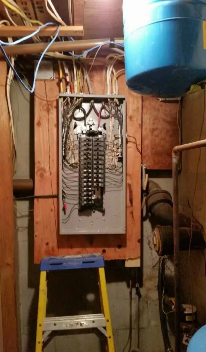 A ladder is sitting next to a electrical box in a basement.