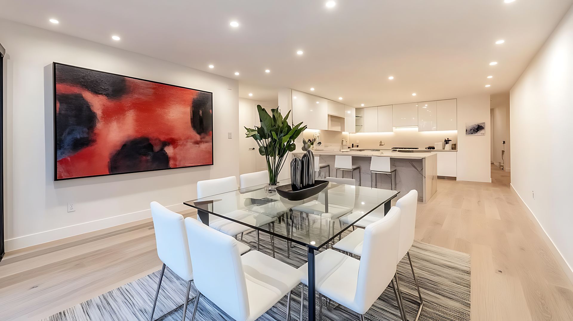 Dining room with glass table, white chairs, abstract red artwork, and open kitchen.