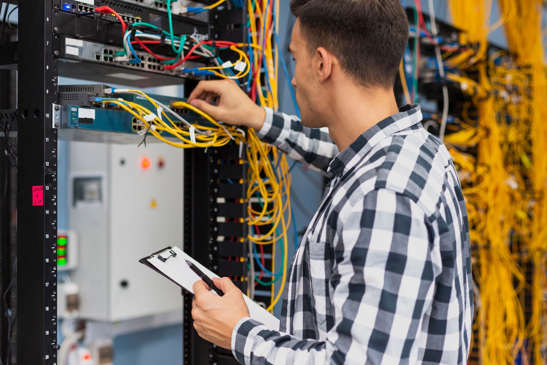 A man is working on a server in a data center while holding a clipboard.