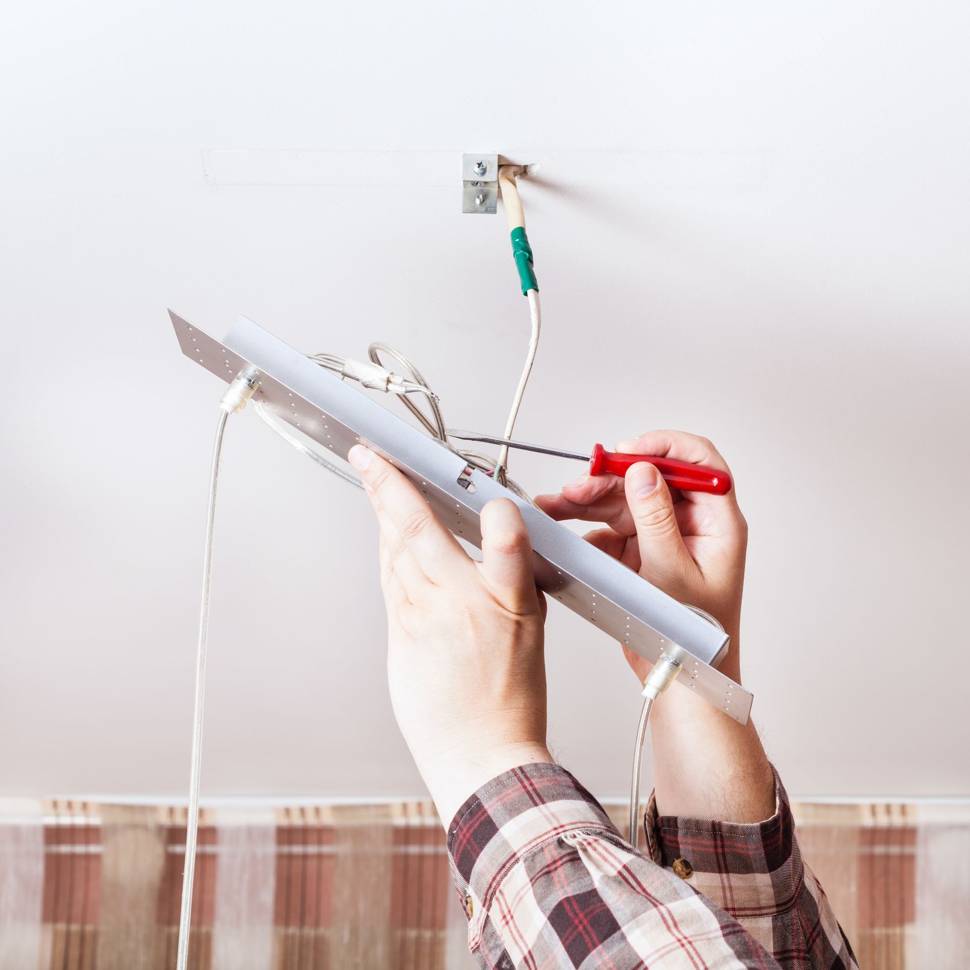 A person is fixing a light fixture with a screwdriver.