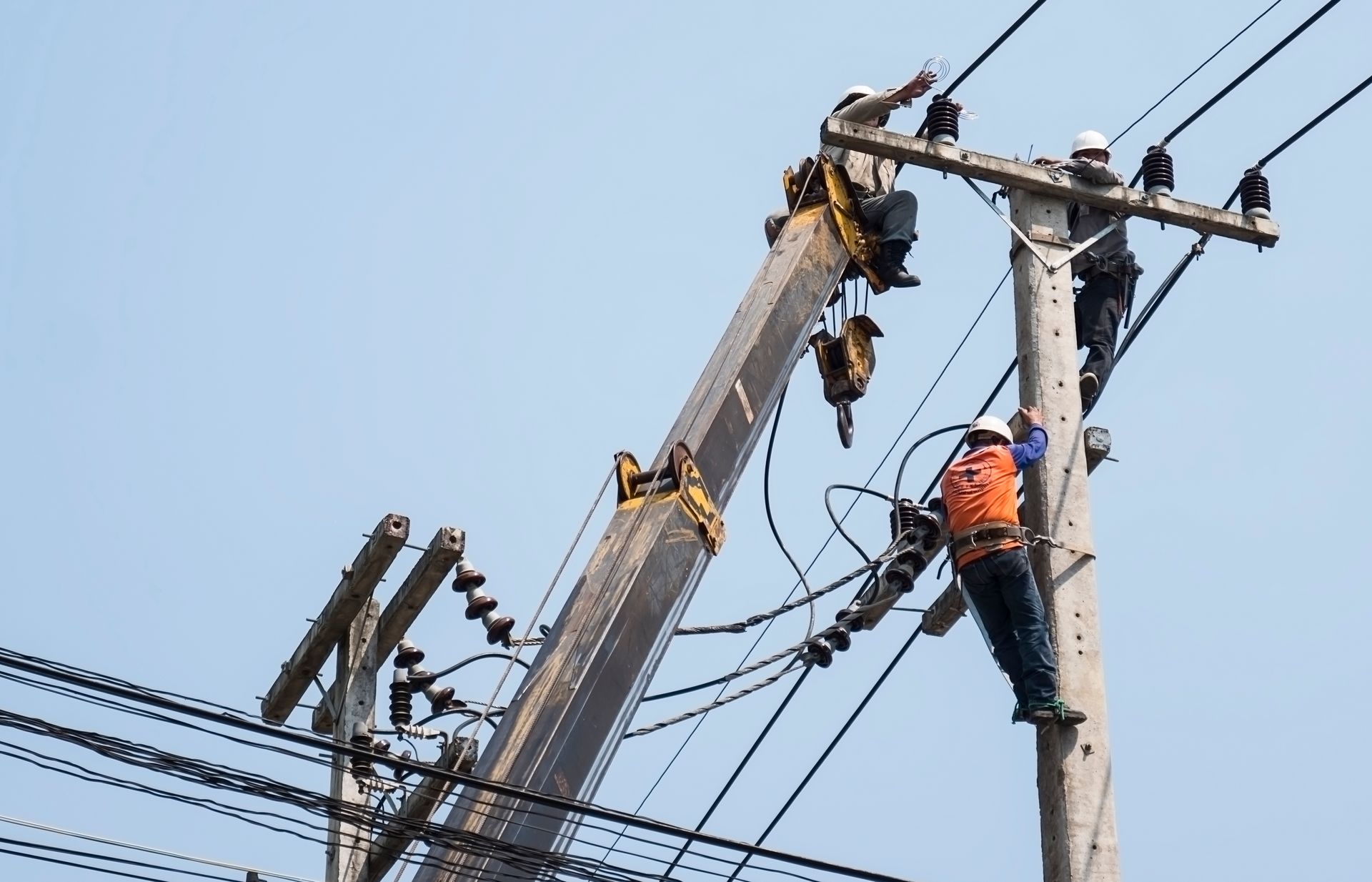 A man is climbing a power pole with a crane attached to it.