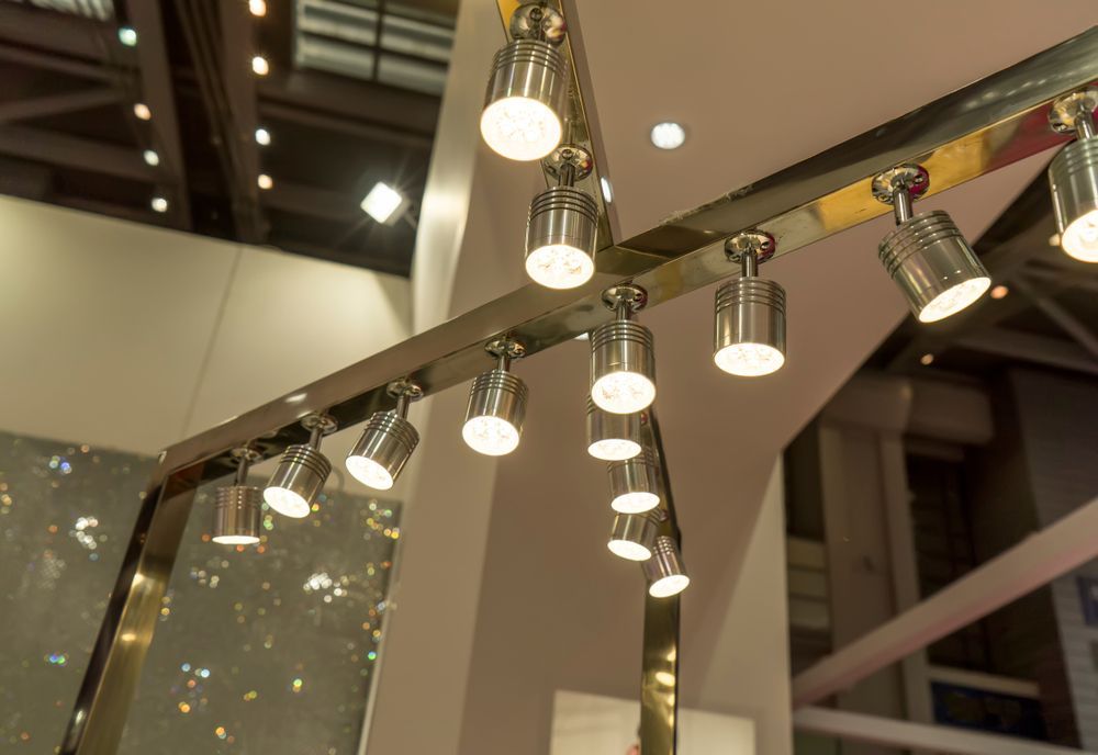 Close-up of a track lighting system with multiple bright spotlights on a gold colored beam.