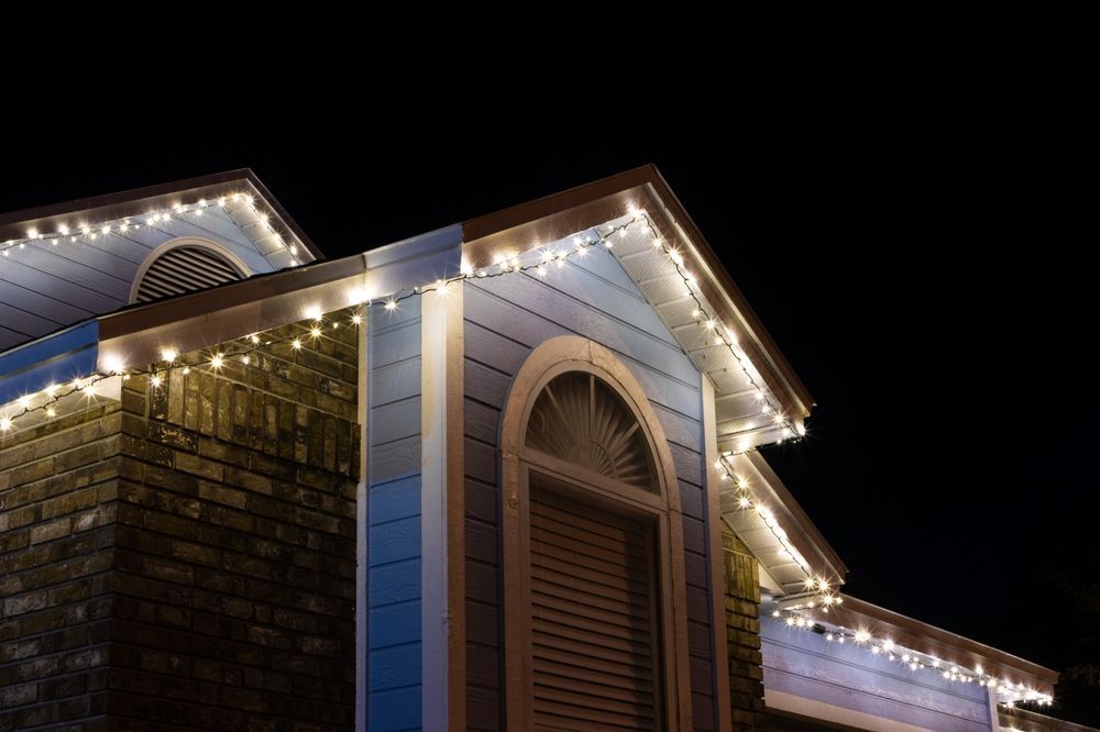 Blue house with Christmas lights outlining roof against a dark night sky.