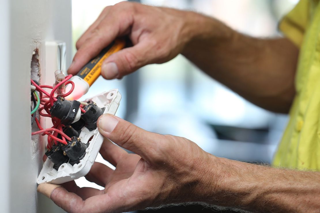 A man is working on an electrical outlet with a screwdriver.