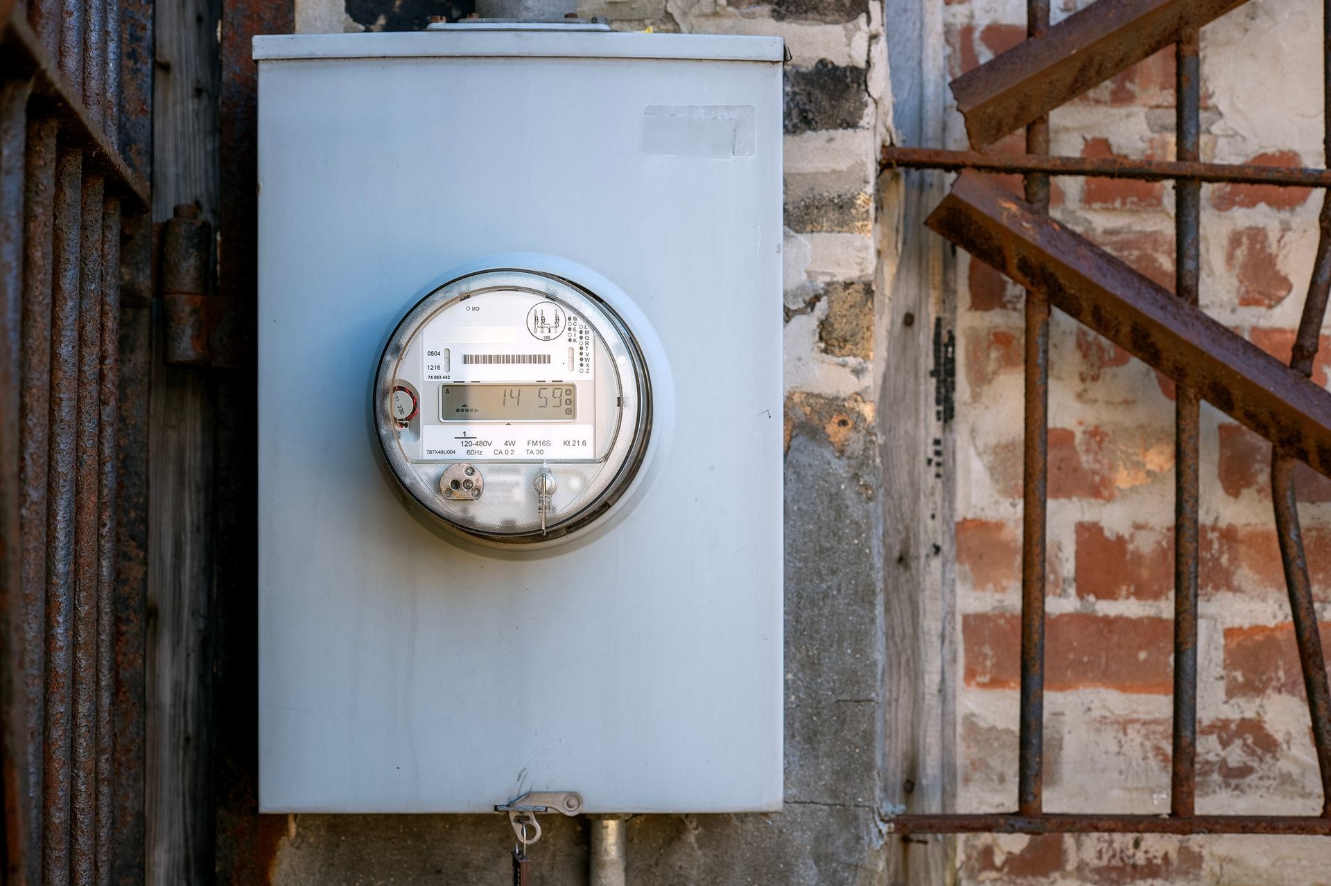 An electric meter is mounted on a brick wall next to stairs.