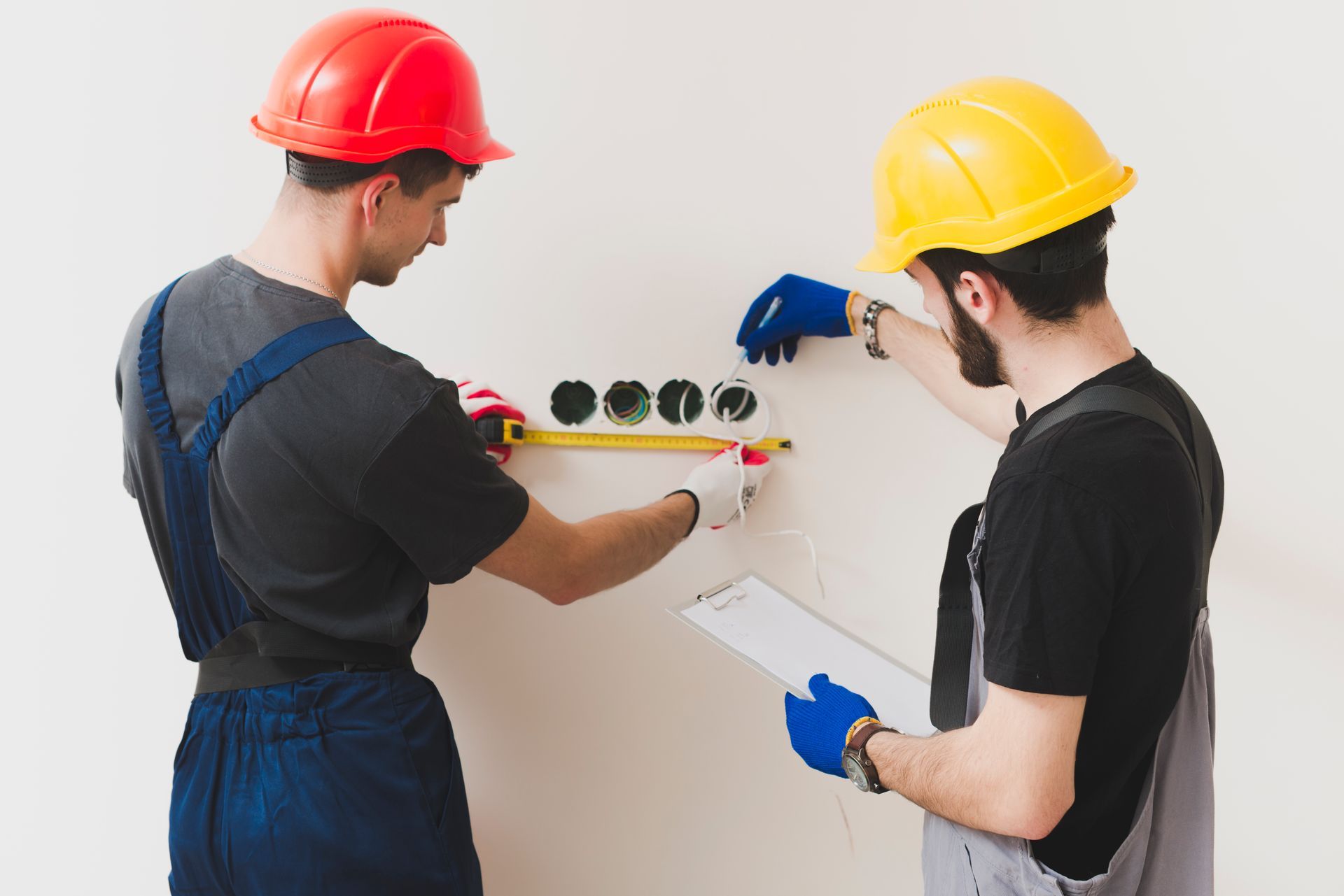 Two construction workers are measuring a wall with a tape measure.