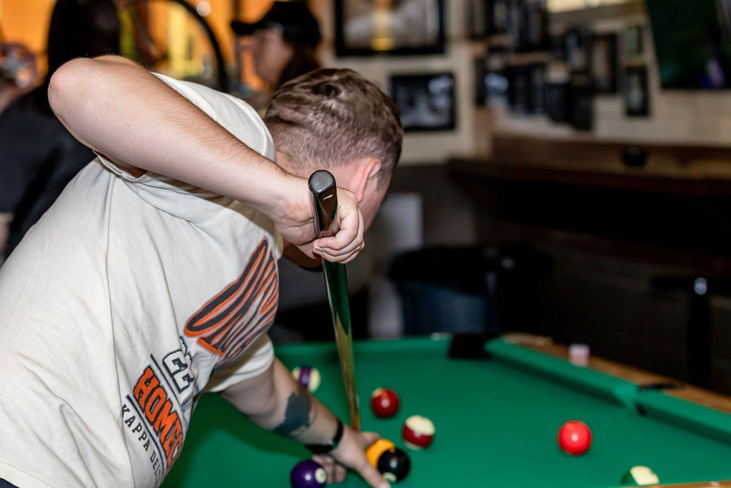 A person playing pool, aiming with a cue stick over a green felt table. Other balls are visible.