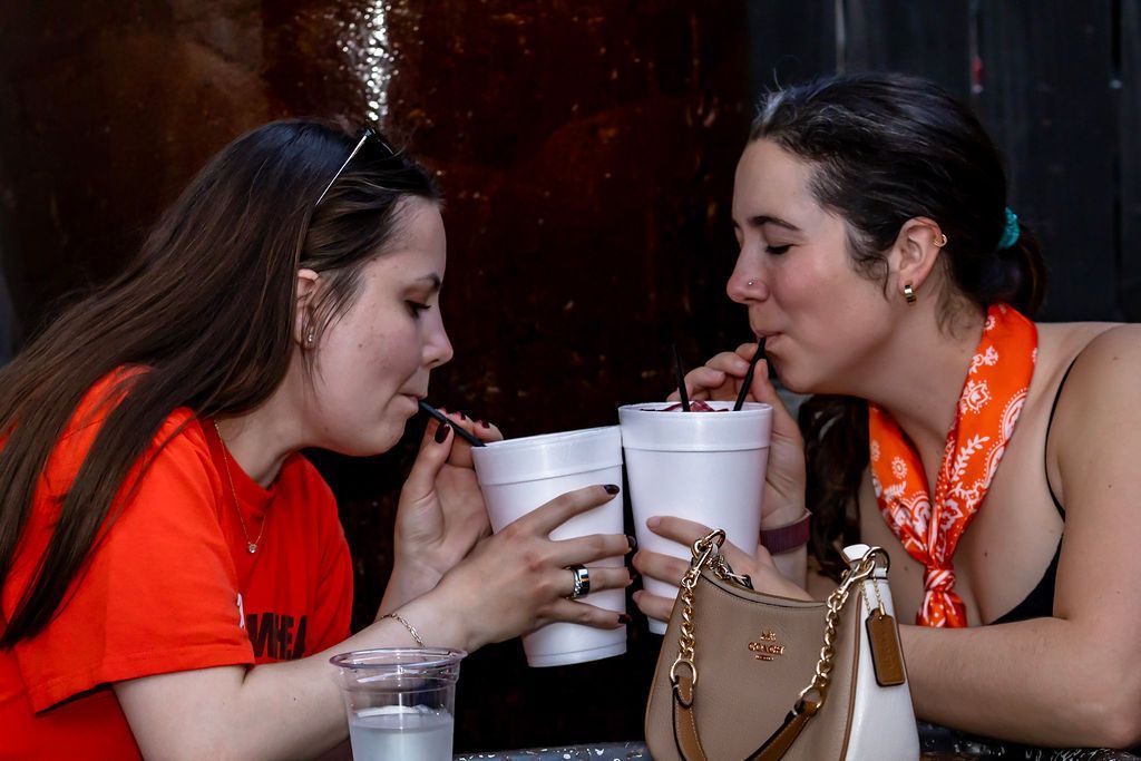 Two people are drinking from cups with straws. Orange shirts, outdoor setting.