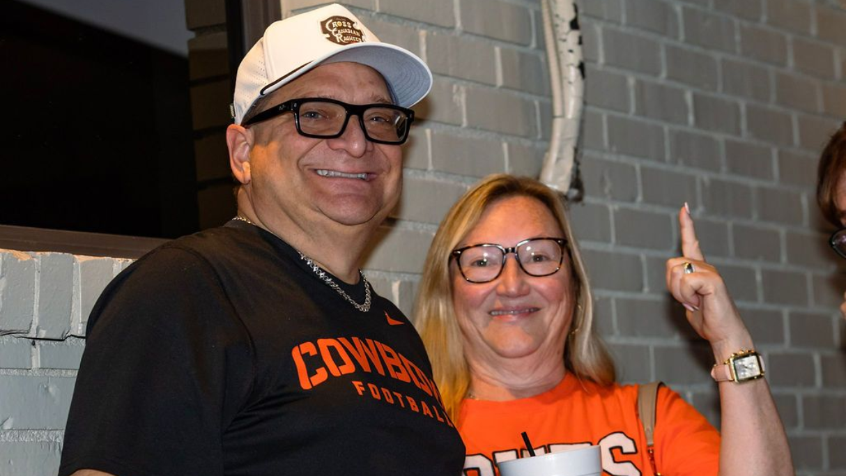 Man and woman smiling, wearing glasses and orange