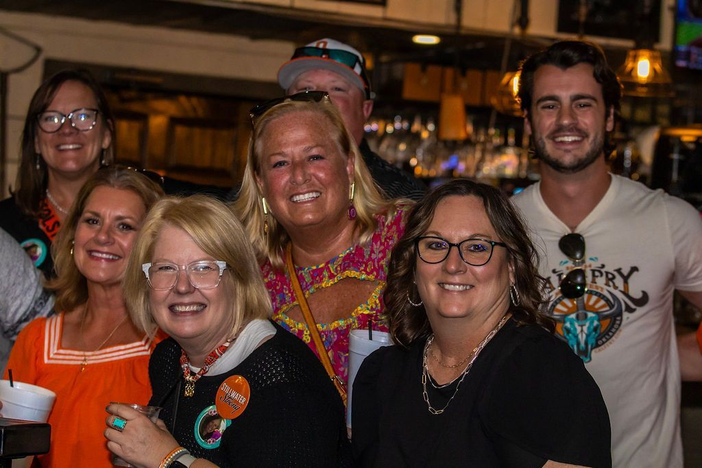 Group of smiling people pose indoors, inside the bar; some wear glasses and colorful shirts.