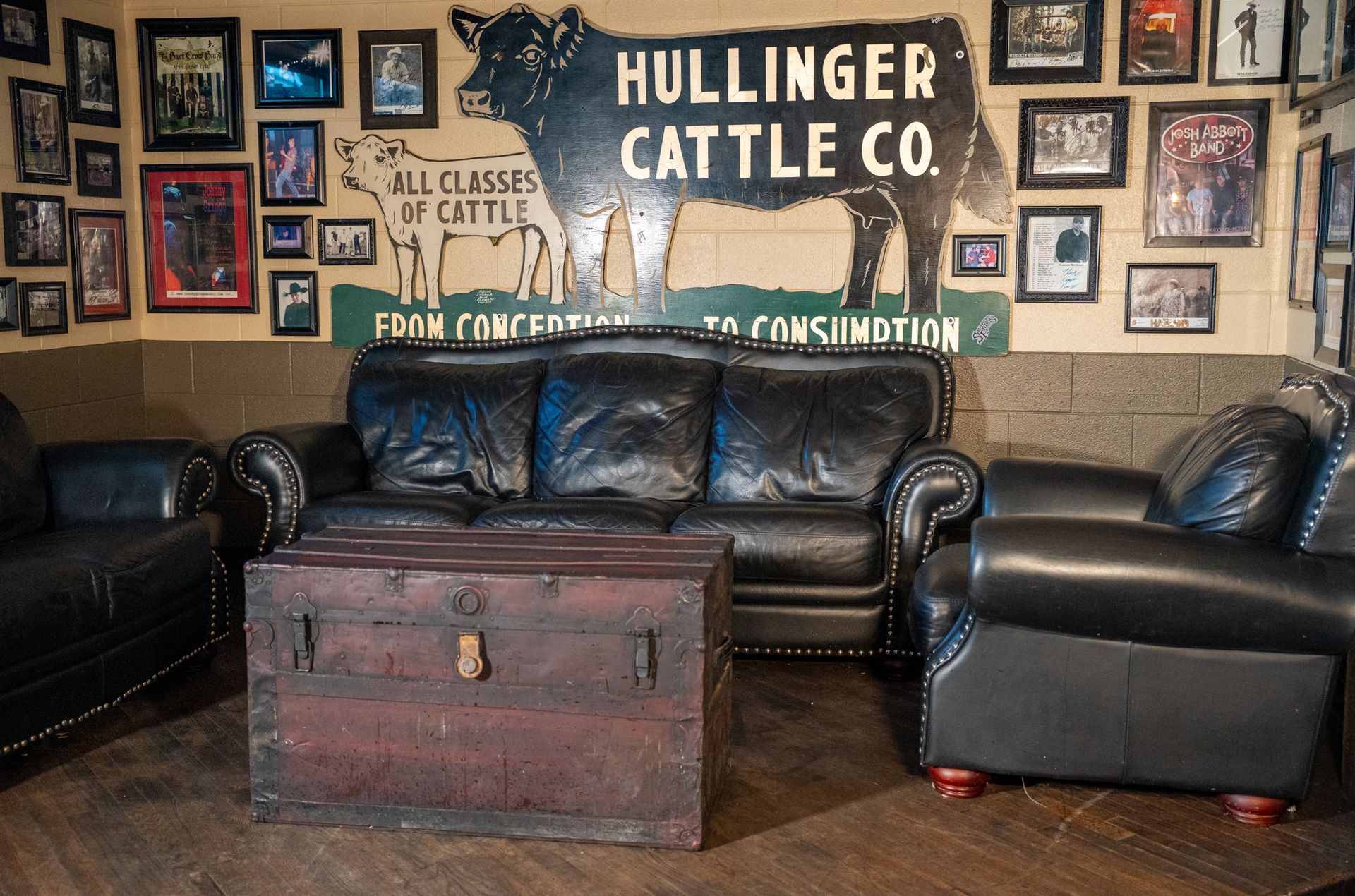 A rustic lounge area with leather furniture, an antique trunk coffee table, and a cattle company sign.