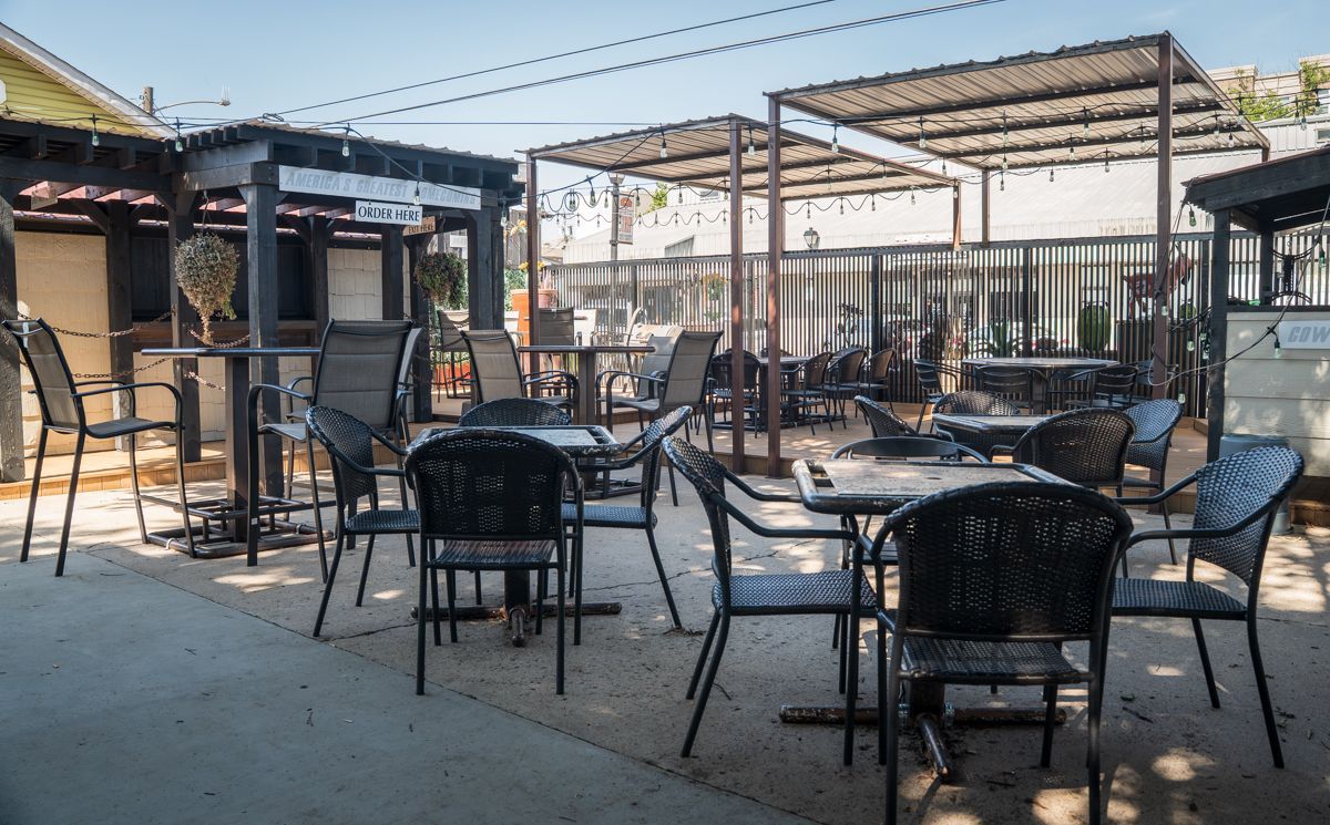 Outdoor patio with tables and chairs under a pergola, ready for customers.