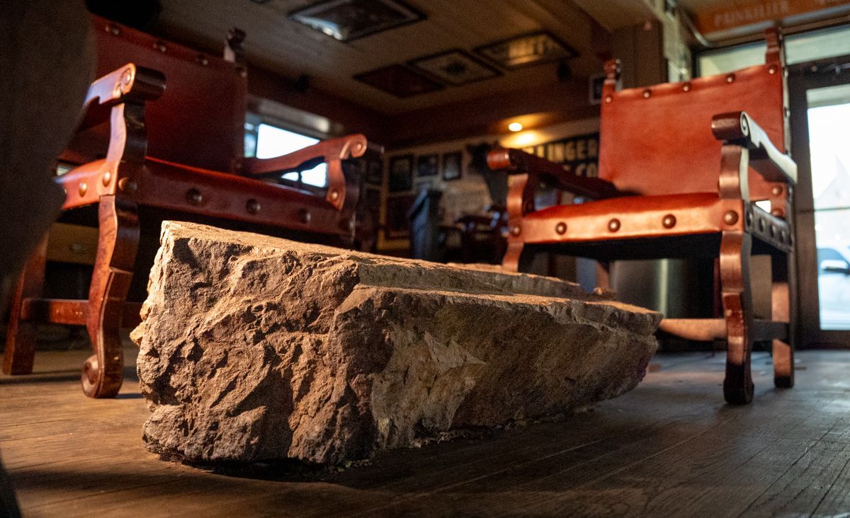 Rough stone bench between two red leather armchairs in an interior space.