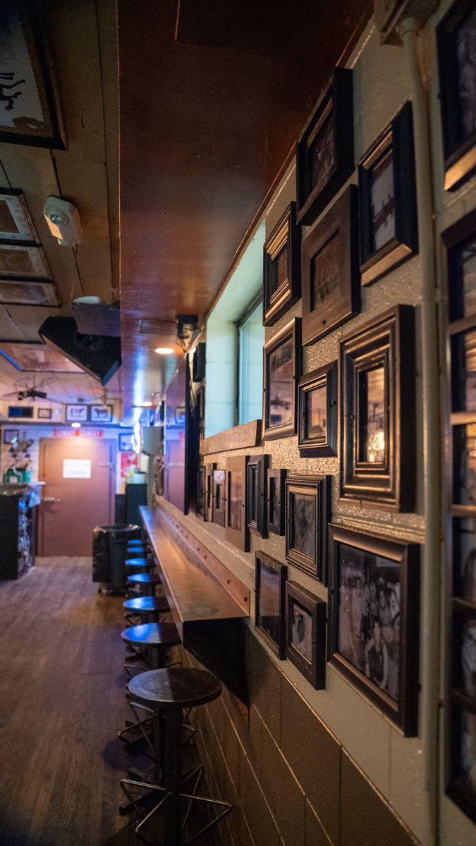 Long, narrow bar with stools, wooden counter, and framed photos on the wall.