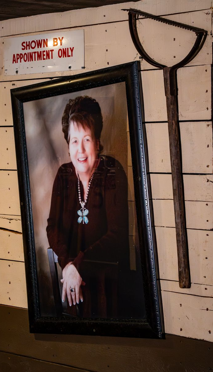 Penny's portrait in black frame on wooden wall next to a rusty tool; sign reads 