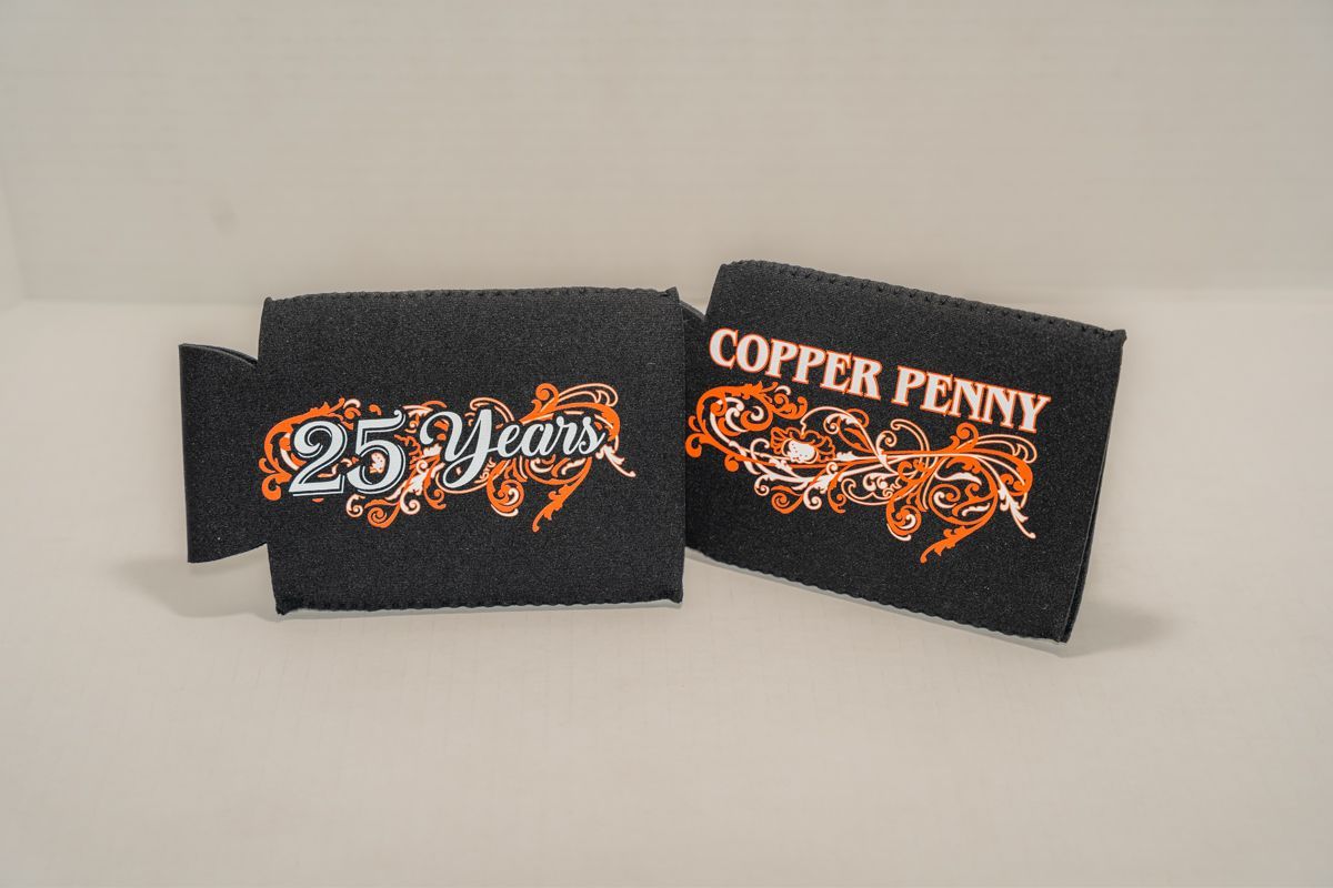 Two black can coolers with embroidered logos: "25 Years" and "Copper Penny" with orange designs.