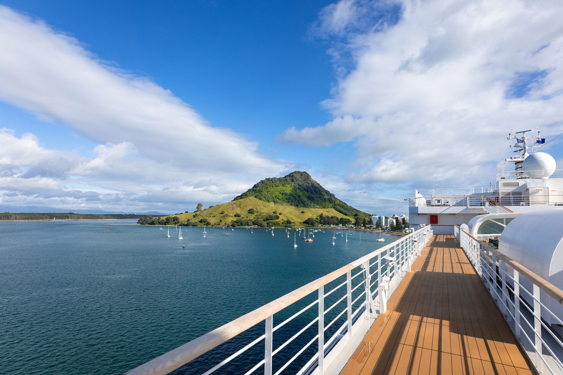 Cruise ship deck with a mountain island in the blue sea under a partly cloudy sky.